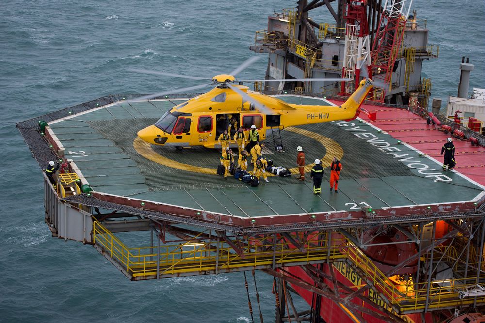 An Airbus H175 helicopter is shown on a helipad with oil and gas workers nearby. 