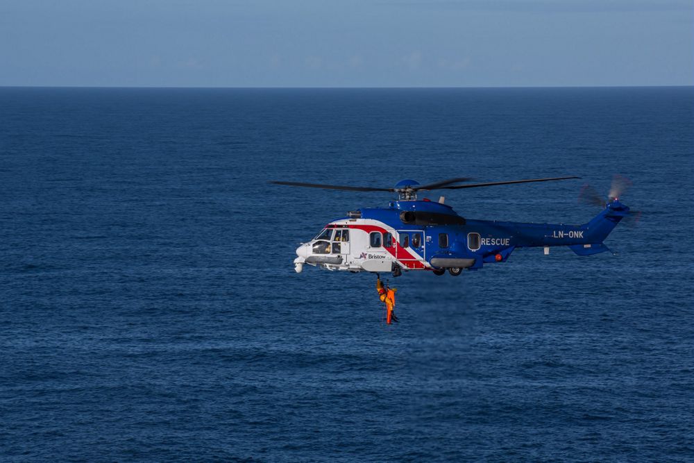 Side view of an Airbus H225 helicopter flying over a body of water. 