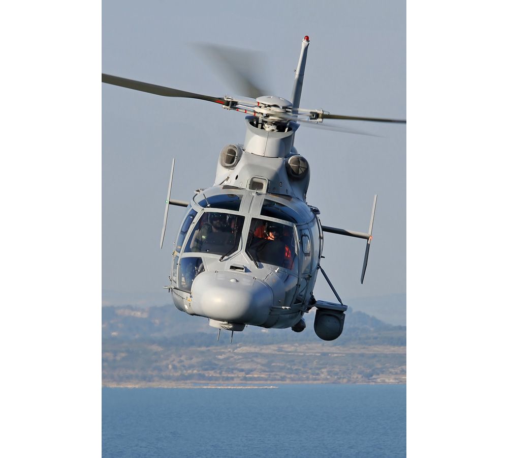 Head-on view of an Airbus AS565 MBe helicopter flying over water. 