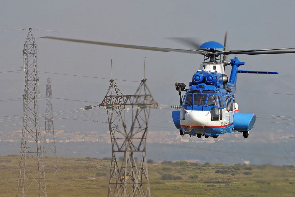 Head-on view of an in-flight Airbus H225 helicopter with power lines in the background.  