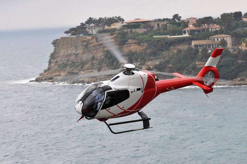 Side view of an Airbus H120 helicopter flying over water.  