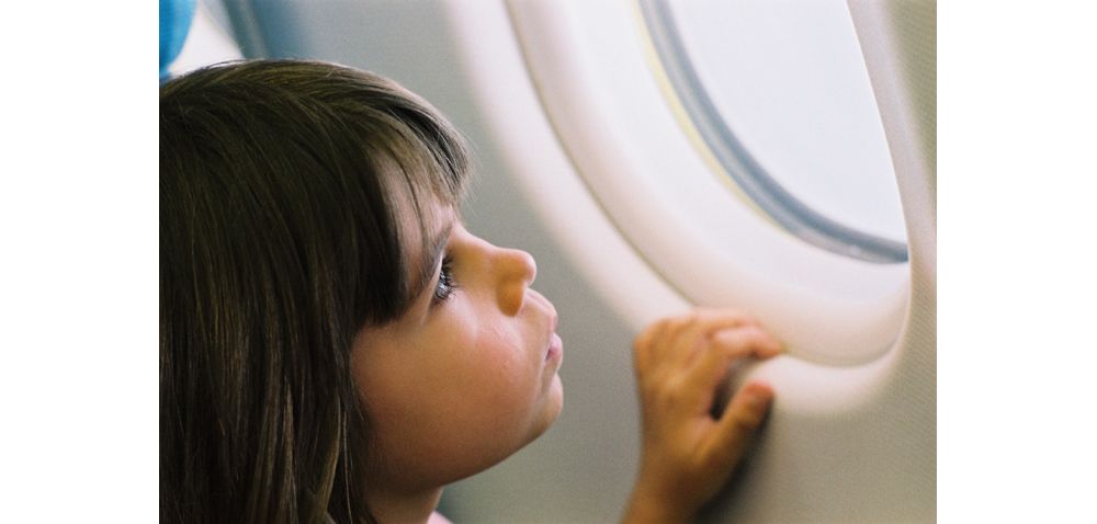 A young girl looks out the passenger window of an Airbus commercial aircraft.   