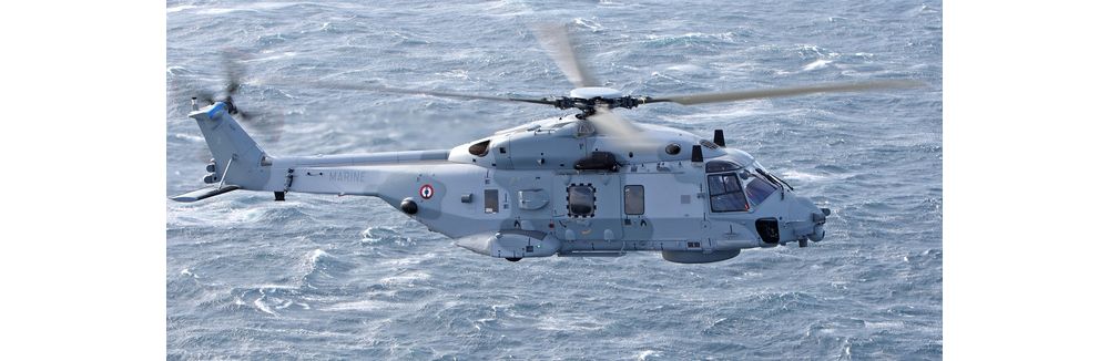 Side view of an NH90 NFH military helicopter flying over water. 