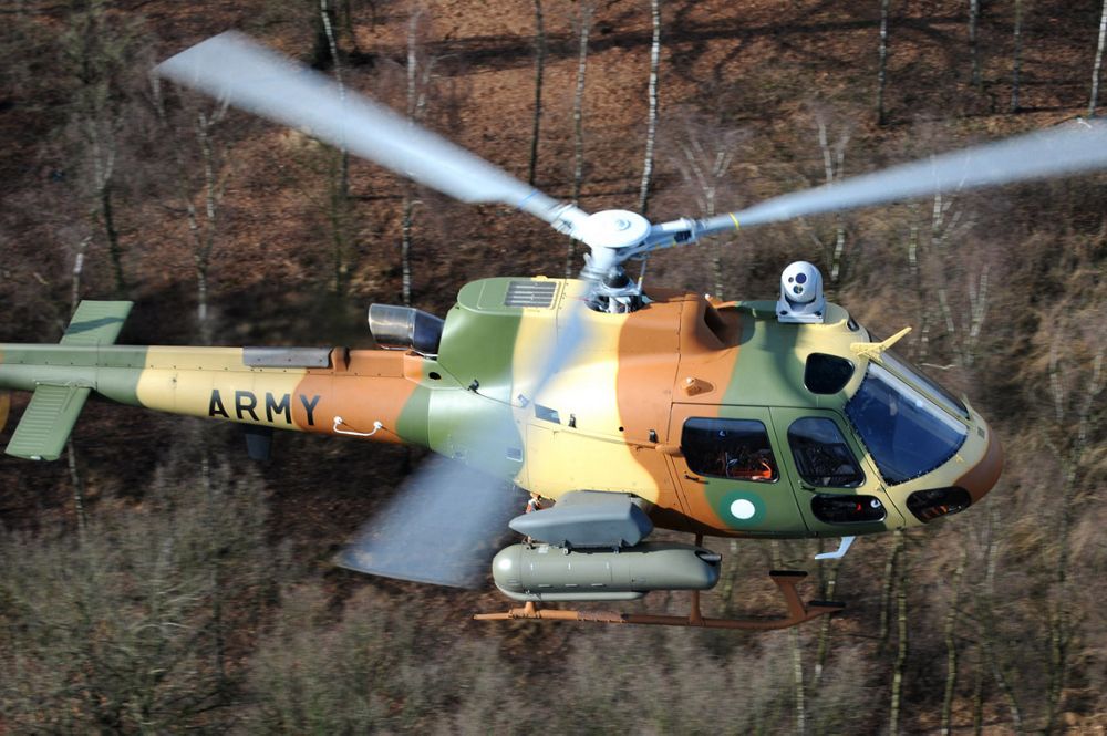 Aerial view of an H125M military helicopter flying over a wooded area. 