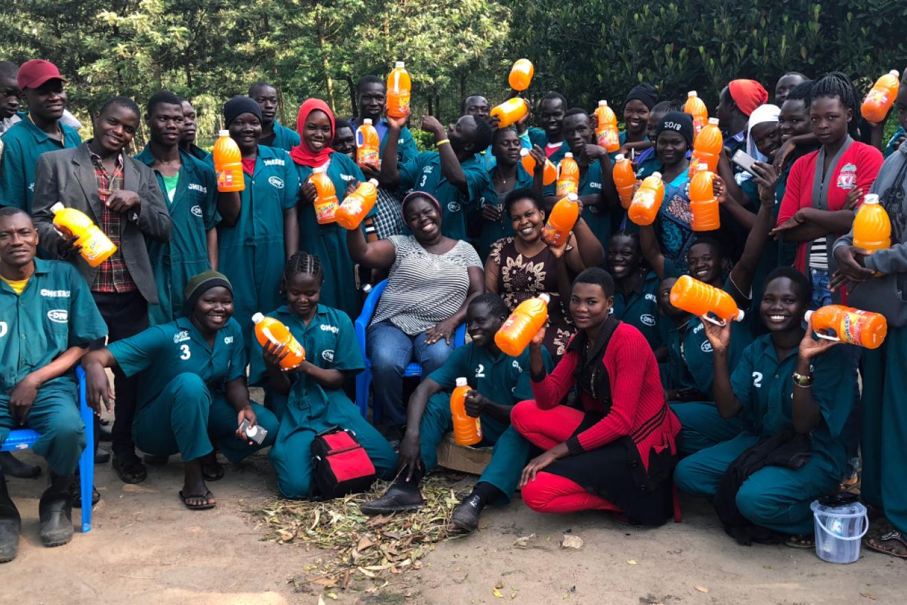 A group poses for a photo holding out orange juice jugs.