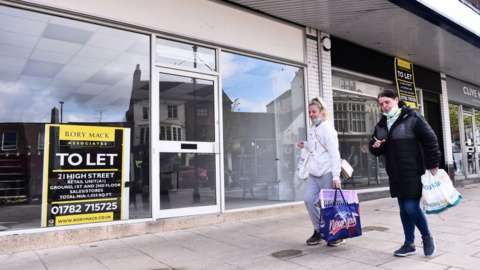 Women walk past empty retail units with To Let signs