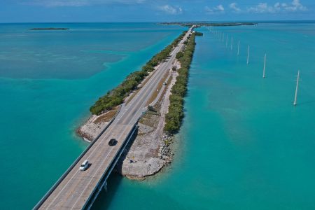 Highway going across small strip of land on top of large blue body of water.