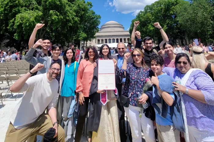 A family excitedly cheers around their graduate holding her diploma