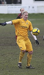 Soccer player Alicia Ferguson, wearing a yellow kit, prepares to control a ball during a match.