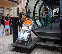 A woman with a baby carriage uses a platform lift to access a station above street level