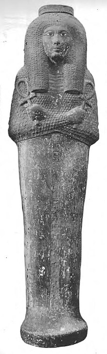 An Egyptian coffin with the carved image of a woman's face and body on the lid. Her arms are crossed, and she is portrayed as holding an ankh in each hand (a key of life symbol, shaped like a "T" with a loop on top).