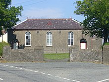 single storey rendered building with slate roof, door and three arched windows