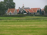 About 10 small buildings of dark wood with steeply peaked red roofs. In the center is a larger building with a grey roof and a small clock tower.