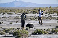 Two members of the recovery team examine the return capsule after landing