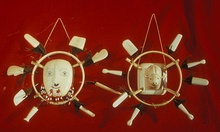 Photo of two masks: In the center is the image of a face, surrounded by a ring, in turn surrounded by eight white rectangular pieces.