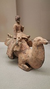 Many objects suggesting exchanges with Central Asia have been found, especially in Northern Wei tombs. Left: Model of a Silk Road camel driver, Northern Wei period. Right: a Kushano-Sasanian style plate with hunting scene, from the Northern Wei tomb of Feng Hetu (封和突, a Xianbei military official, 438–501) in Xiaozhan village, Datong. Shanxi Museum.[45][11]: 152 
