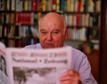 An image of Gerhard Frey reading the newspapers with a backdrop of books