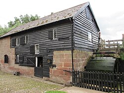 Stone mill building with weatherboarding and waterwheel to right