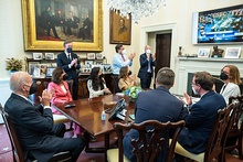 Photo of Biden and staffers, seated, looking at a television
