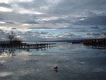 A crow walks on a frozen lake near a narrow dock.