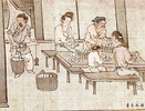 Two women, two men and a child sit at a table, sorting white cocoons in baskets.