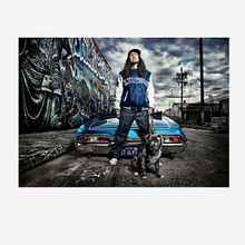 Yankovic in a blue Lynwood jacket standing beside a low-rider convertible with a pit bull on a graffitied urban street scene