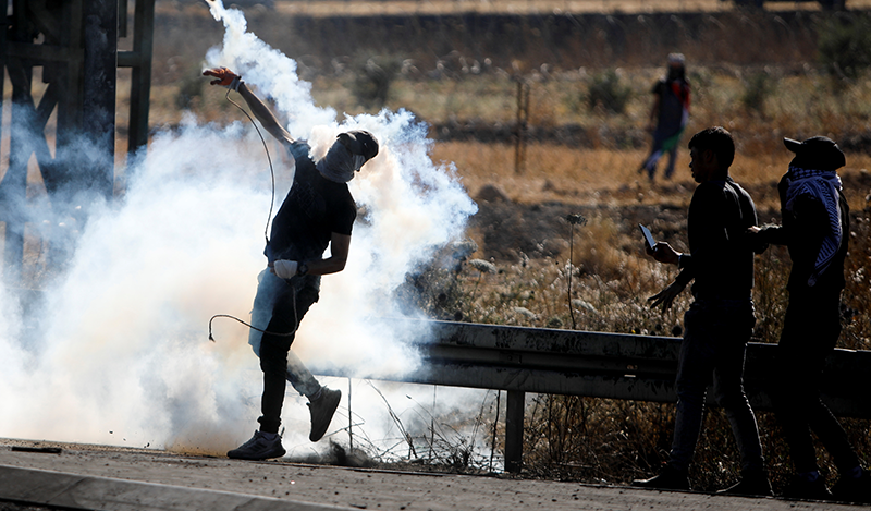A Palestinian protestor throws a tear gas grenade at Israelis during an anti-Israel protest over cross-border violence between Palestinian militants in Gaza and the Israeli military, near Hawara checkpoint near Nablus in the West Bank, May 18, 2021. REUTERS/Raneen Sawafta
