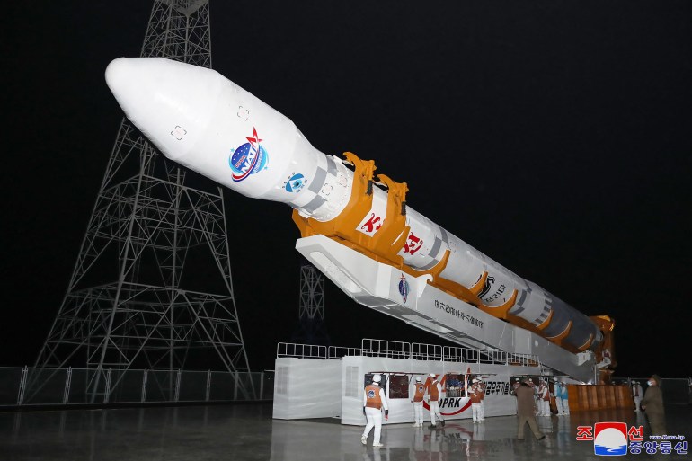A rocket carrying the reconnaissance satellite 'Malligyong-1' on its transporter. The rocket is white.