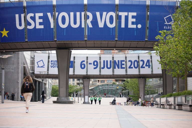 People walk near signs for the upcoming EU elections, at the European Parliament in Brussels, Belgium