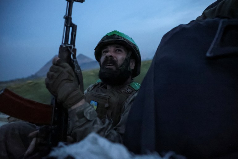 A Ukrainian soldier looking up at the sky. He is sitting in a car and has his weapon ready at his side.