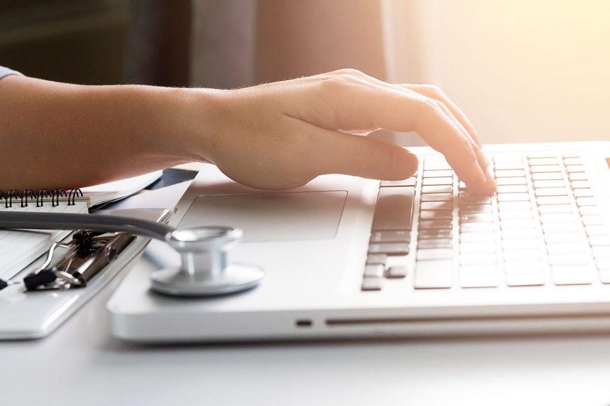 Hand on a laptop with a stethoscope nearby