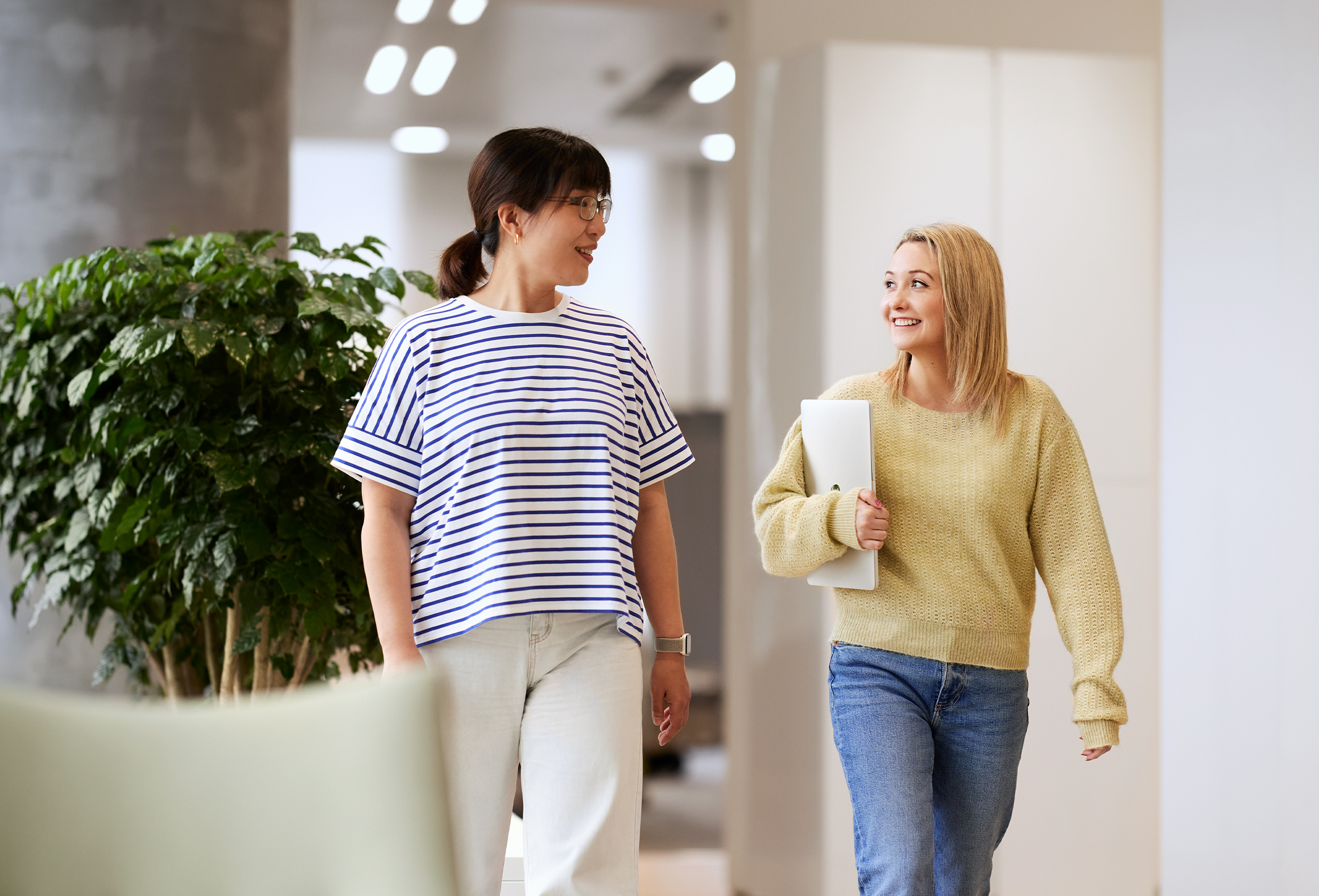 Two Apple employees smiling in conversation, walking through a brightly lit common space.