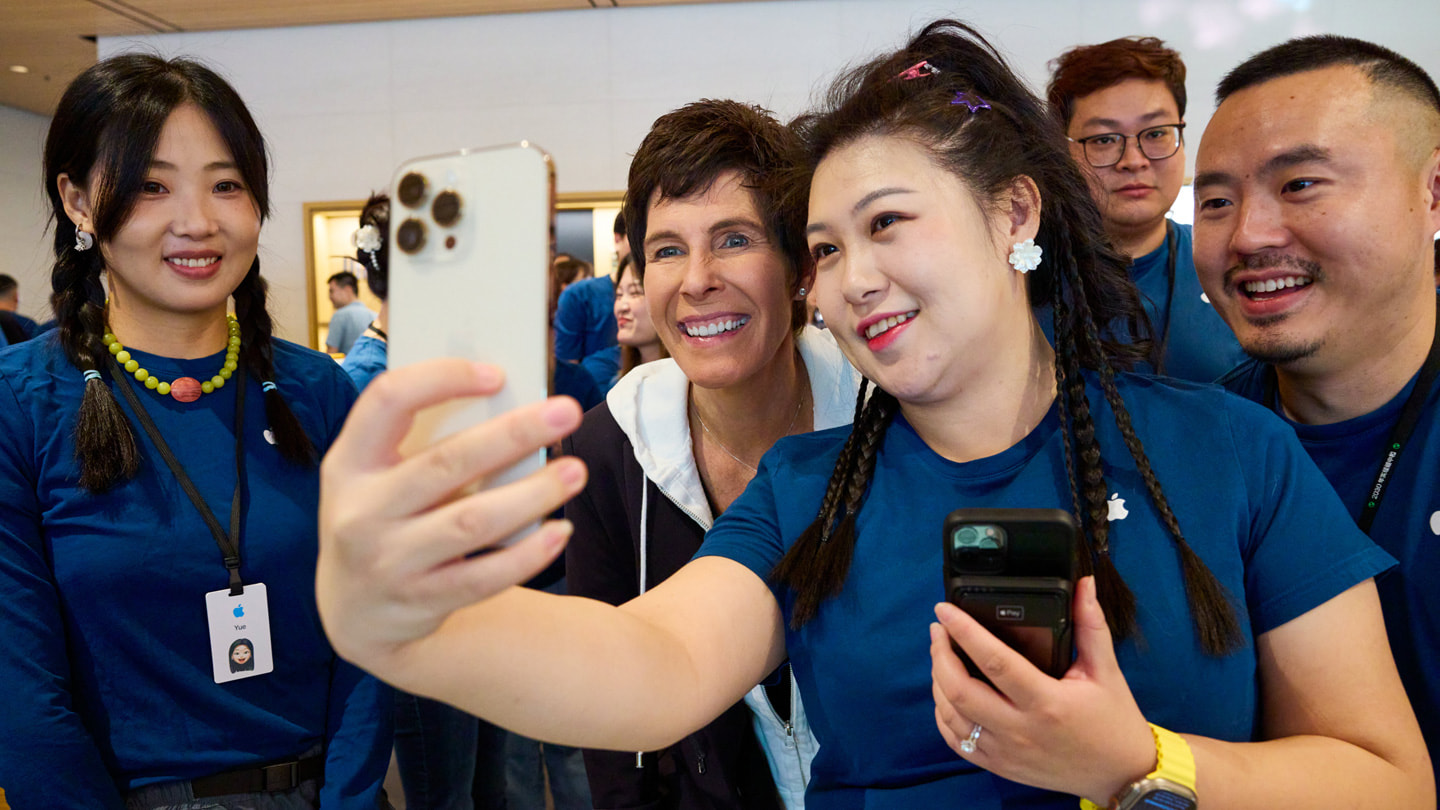 إحدى أعضاء الفريق تلتقط صورة سيلفي مع ديردره أوبراين وآخرين من أعضاء الفريق باستخدام iPhone 15 Pro باللون الأبيض.