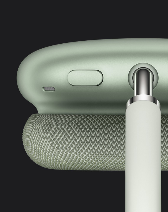 Yksityiskohtainen näkymä vihreiden AirPods Max ‑kuulokkeiden kuulokekupin yläosassa, yläsangan kiinnityskohdan vieressä olevasta Melunhallinta-painikkeesta.