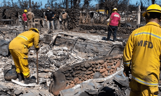 Two firefighters in yellow in a burned out house in Lahaina, Maui