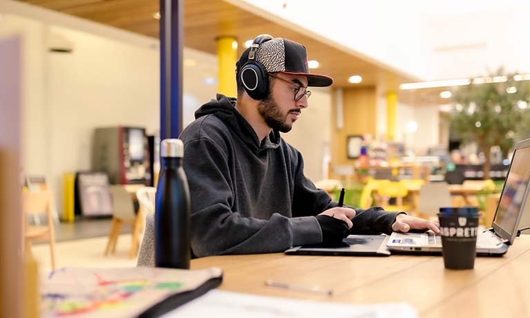 A postgraduate student working on his laptop while listening to music.