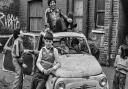 Children at play by derelict car dumped at Fieldgate Mansions in Whitechapel that David snapped in the 1970s