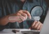 Man holding magnifying glass while using computer