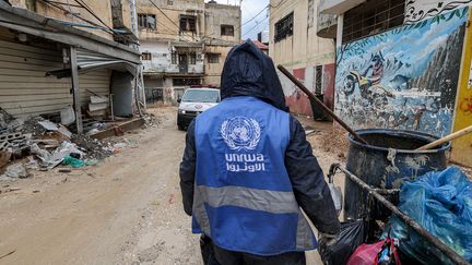 Un homme ramasse des déchets alors qu'il porte une veste portant le logo de l'Office de secours et de travaux des Nations Unies pour les réfugiés de Palestine dans le Proche-Orient (UNRWA), à Jénine, en Cisjordanie occupée, le 30 janvier 2024. (JAAFAR ASHTIYEH / AFP)