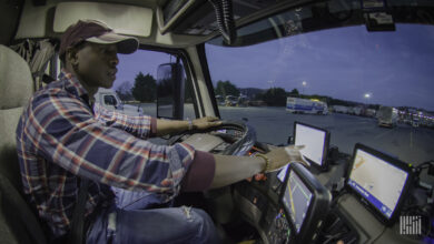 Man sits behind the steering wheel in the cab of a semi truck, touching the screen of a tablet on the dashboard