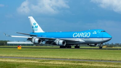 An all-blue KLM Cargo jumbo jet rolls down the runway under a blue sky.