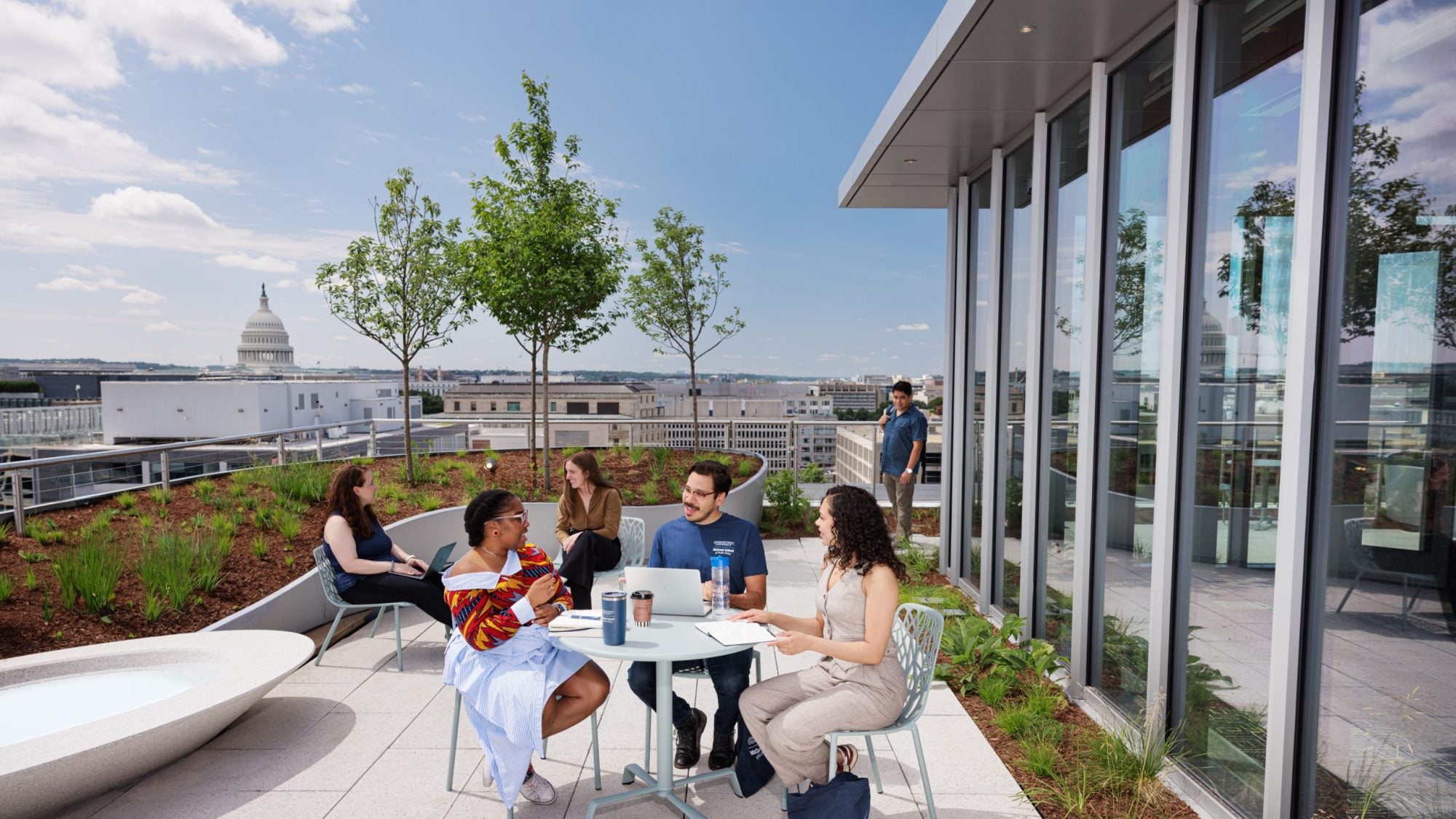 Students at a table talking while on a terrace with the US Capitol in the background.