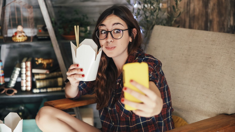 woman taking video of herself eating from food container