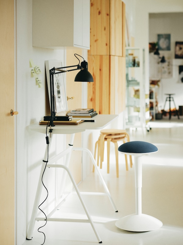 A workstation in a space with white walls, floors, desk and NILSERIK standing support with Vissle blue-coloured seating.