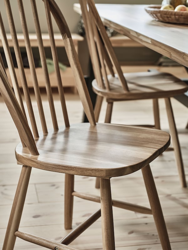 In a dining room are two bare SKOGSTA wooden chairs in solid acacia placed by a SKOGSTA dining table in a light-filled space.