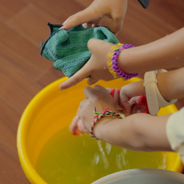 Two young girls rinse PEPPRIG microfibre cloths in a PEPPRIG bucket.