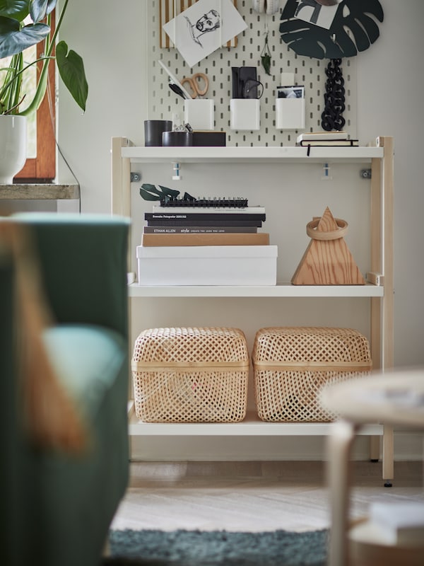 A white and birch shelving unit with storage boxes on the bottom shelf and various desk items sitting on the top shelf