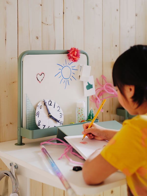 Close-up of young girl at white school desk with green writing board and whiteboard in childrens bedroom with wood walls.