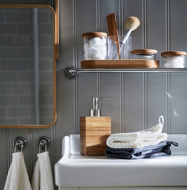 A bamboo DRAGAN soap dispenser is placed next to folded towels on a white shelf in a bathroom filled with spa items.