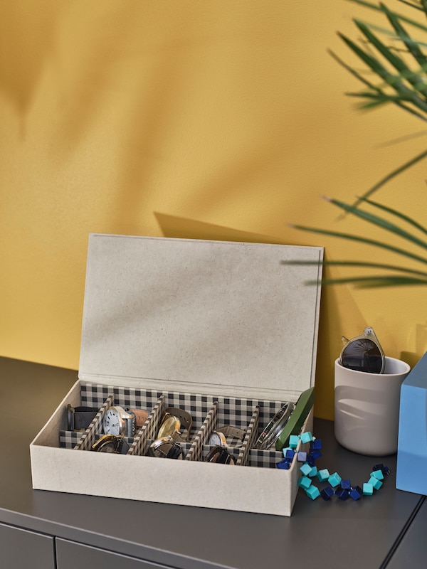 A flat decoration box in beige with a lid and different sections for storing jewellery and small things inside. Lid is open.